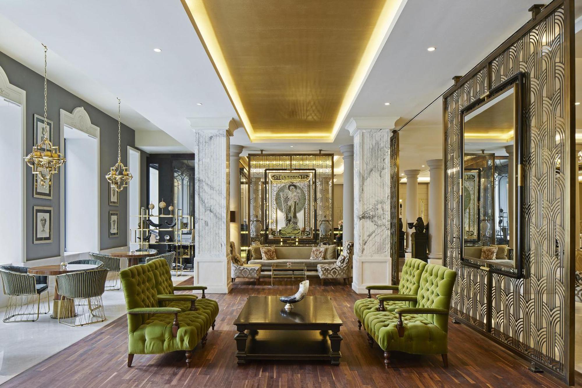 Titanic Gendarmenmarkt Berlín Exterior foto The photo depicts a stylish and elegant interior space, likely a lobby or lounge area. It features tall ceilings with sophisticated lighting and a modern design aesthetic. There are two vibrant green chairs positioned around a dark wooden coffee tabl